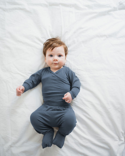 Baby in einem langärmligen, fußbedeckenden Einteiler in Blaubeere. Der Babyknicker Kaschmir-Mix - Blaubeere bietet Wärme und Komfort, ideal für zarte Babyhaut und perfekt für die ersten Lebenswochen.