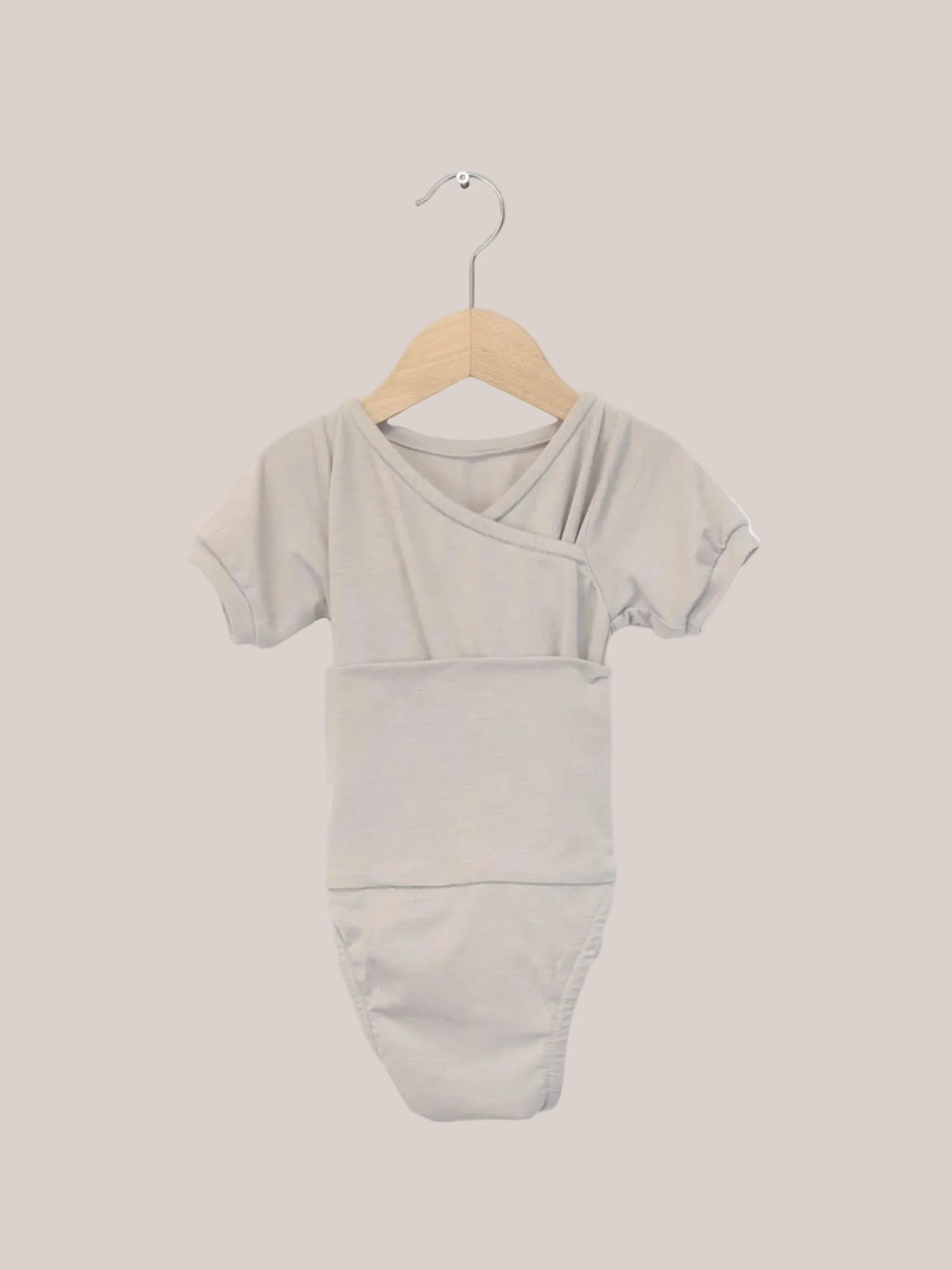Body bébé évolutif à manches courtes en mélange de cachemire, sur un cintre en bois, particulièrement doux et sans boutons, idéal pour faciliter le change et assurer le confort. Cadeau parfait pour bébé.