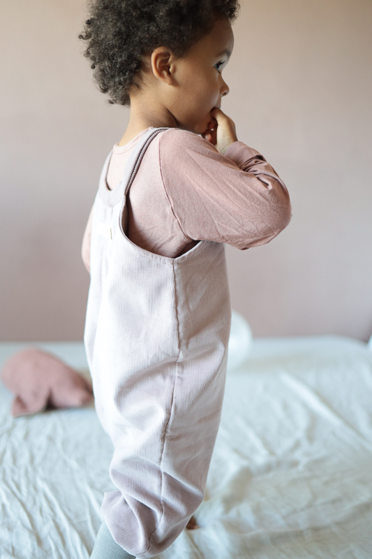 Ein Kleinkind steht auf einem Bett und trägt eine Cordhose für Kinder. 