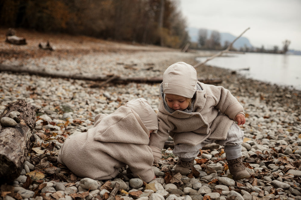 Ein lächelndes Kleinkind mit lockigem Haar, trägt eine Wollwalk Jacke für Kinder und ein Stricktuch von Petit Cochon.
