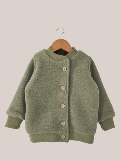 Veste bomber en laine foulée – pistache, présentée sur un cintre en bois, avec doublure en jersey et boutons, fabriquée de manière durable et conçue pour durer par PETIT COCHON.