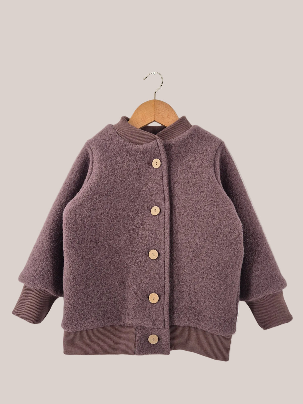 Bomberjacke Wollwalk - Malve, eine Kinderjacke aus Wollwalk mit Knöpfen, auf einem Bügel hängend, zeigt Details wie braune Strickärmel und Holzknöpfe.