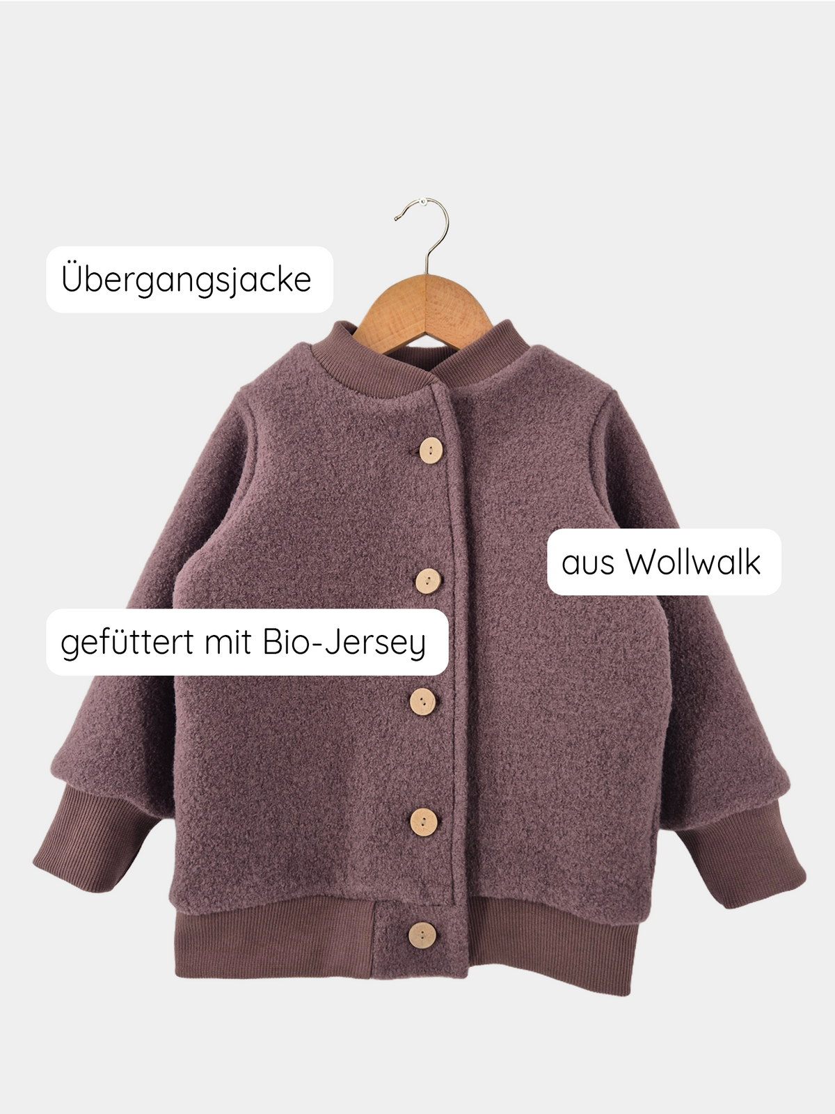Bomberjacke Wollwalk - Malve auf einem Holzkleiderbügel, mit Knöpfen und weichem Jerseyfutter, gezeigt auf einer Schaukel. Nachhaltig in Berlin produziert, bietet sie Wärme und Langlebigkeit für Kinder.