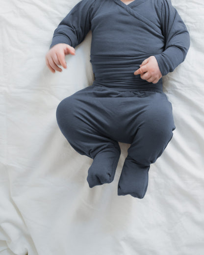 Baby in einem Babyknicker Kaschmir-Mix - Blaubeere, einem gemütlichen, langärmeligen Fußanzug. Der Onesie hat praktische Umklappbündchen, die Wärme bieten, ideal für die empfindliche Haut Neugeborener.