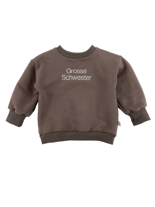 Der Pulli Bio Sweat Praline Gr 1Y zeigt einen kleinen, braunen Crewneck-Sweatshirt mit weißen Stickereien „Grosse Schwester“ vorne, ideal für Kleinkinder, mit gerippten Bündchen und Saum.