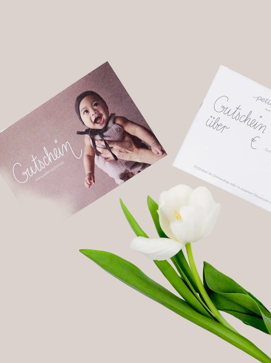 (Kopie) Geschenkgutschein: Zwei Gutscheinkarten, eine mit lächelndem Baby, eine zum Ausfüllen, neben einer weißen Tulpe. Einlösbar online und in Berlin-Tempelhof.