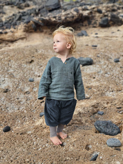 Bambino piccolo in knickerbocker di velluto a coste fine a righe - mirtillo, comodi pantaloni di velluto a coste con bordo a righe, ideali per la libertà di movimento, in piedi su una spiaggia sabbiosa, perfetti per piccoli esploratori e piccole esploratrici attivi.