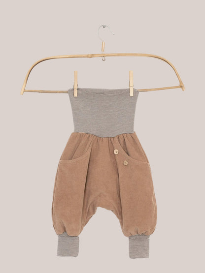 Knickerbocker Feincord Ringel - Weizen: tutina intera con bordo a coste a righe, gamba dei pantaloni in velluto a coste marrone, tasche laterali, bottoni in legno a levetta e polsini a righe, presentata su una gruccia di legno davanti a uno sfondo neutro.
