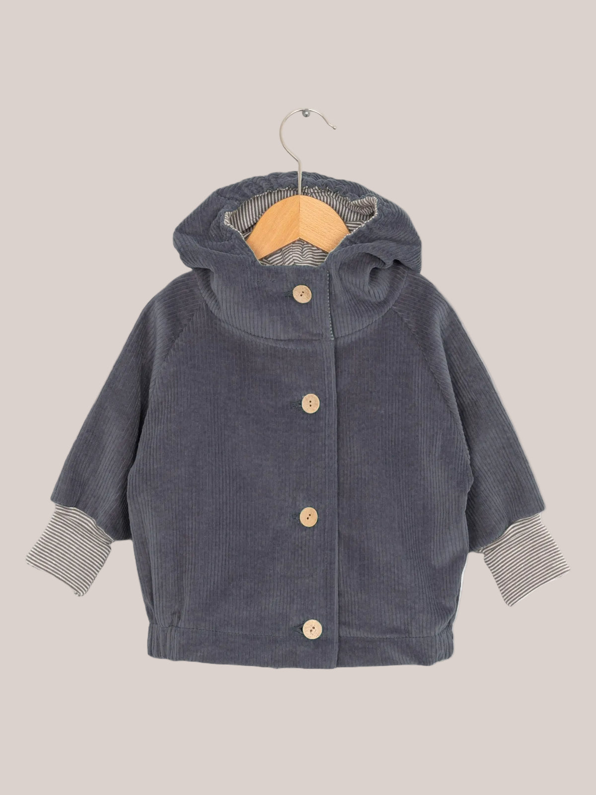 Wichteljacke Breitcord - Denim auf einem Holzbügel, mit Ringel-Armbündchen und Wichtelkapuze, aus weichem Cord für komfortables Tragen, handgefertigt in Deutschland.