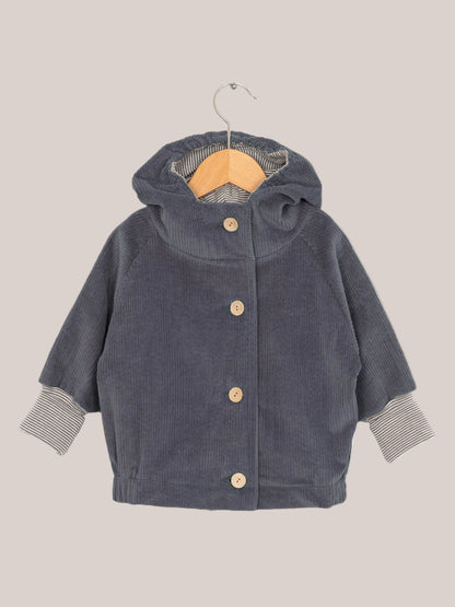 Wichteljacke Breitcord - Denim auf einem Holzbügel, mit Ringel-Armbündchen und Wichtelkapuze, aus weichem Cord für komfortables Tragen, handgefertigt in Deutschland.