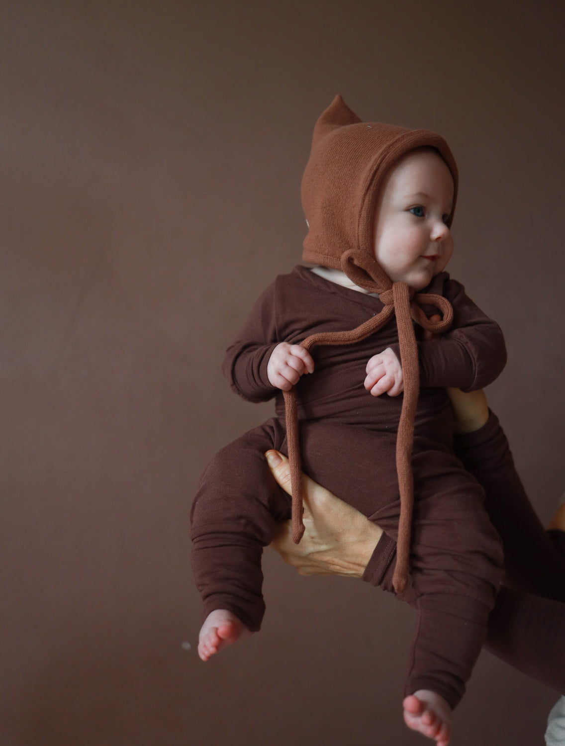 Il bebè indossa un berretto da gnomo lavorato a maglia – color torrone, realizzato in cotone riciclato, con vestibilità elastica e laccetto, perfetto per l’autunno e l’inverno. Prima dotazione per neonati. Regali perfetti per bebè.