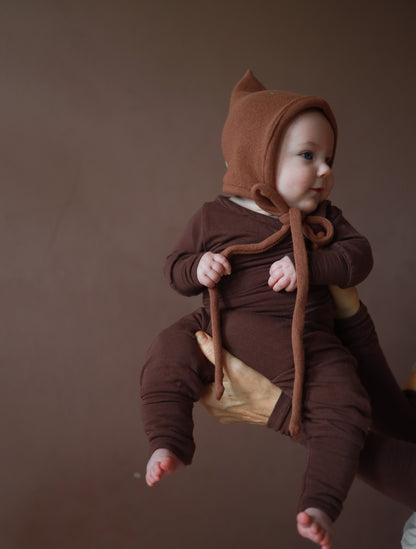 Il bebè indossa un berretto da gnomo lavorato a maglia – color torrone, realizzato in cotone riciclato, con vestibilità elastica e laccetto, perfetto per l’autunno e l’inverno. Prima dotazione per neonati. Regali perfetti per bebè.