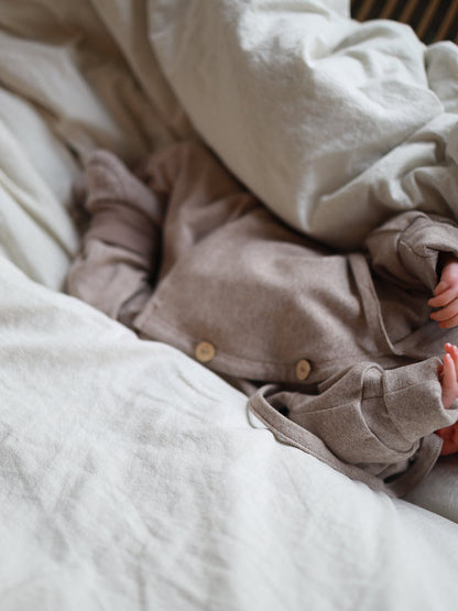 petit cochon Baby Schlüttli aus beigem Feinstrick mit seitlicher Kokosknopfleiste, getragen von einem Neugeborenen