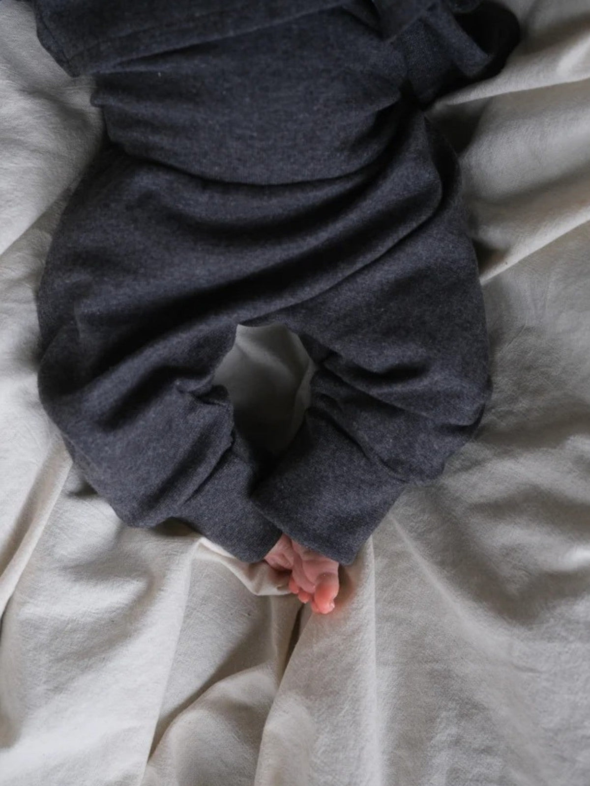 petit cochon Babyknicker aus weichem, dunkelgrau meliertem Feinstrick-Jersey für Babys auf einer hellen Decke