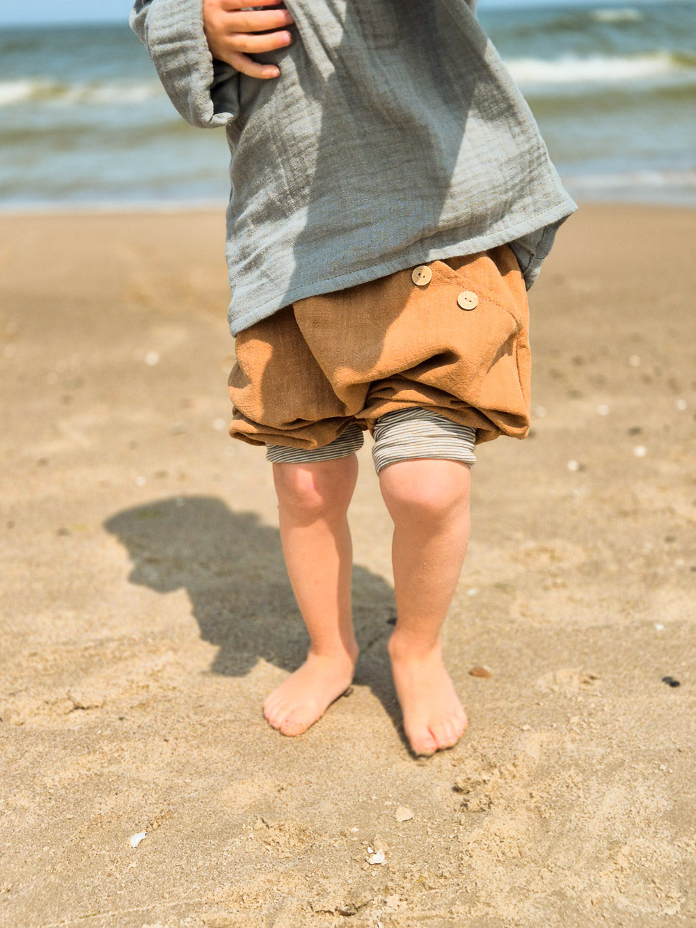 petit cochon Knickerbocker aus braunem Leinen mit Knöpfen, getragen von einem Kind am Strand