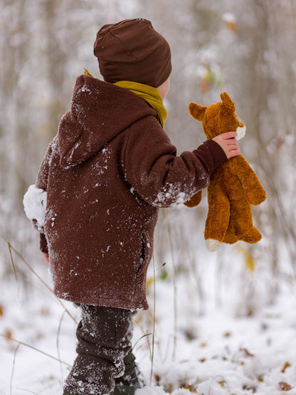 Kind in brauner petit cochon Wollwalk-Wichteljacke mit Kapuze und Bio-Jersey-Futter im verschneiten Wald