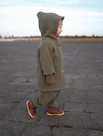 petit cochon Wichteljacke aus olivgrünem Wollwalk mit Kapuze und krempelbaren Bündchen an einem Kind im Freien