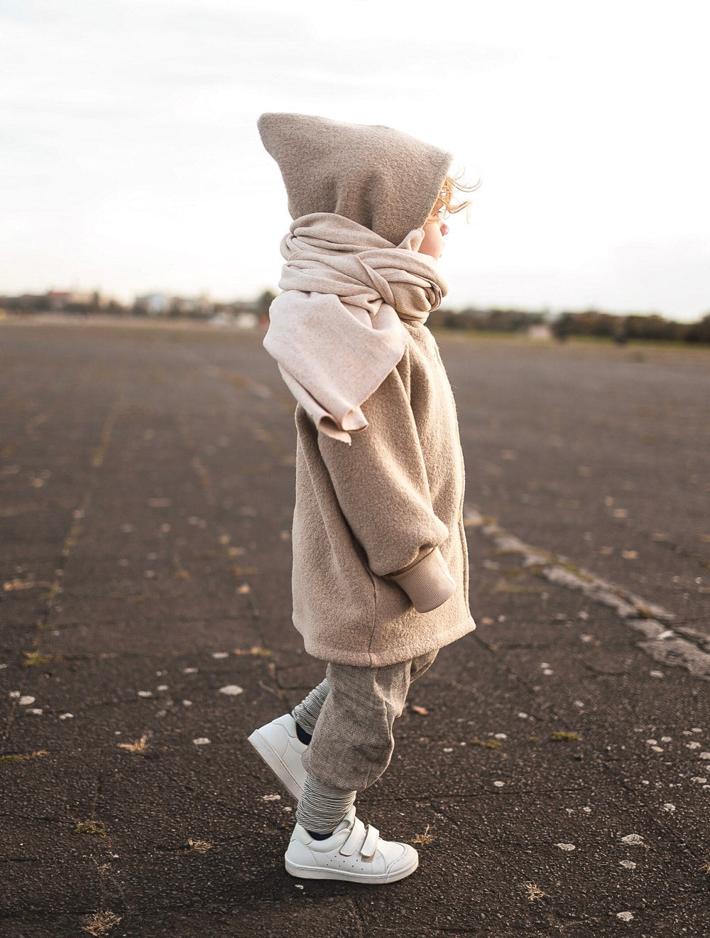 petit cochon Wichteljacke aus beigem Wollwalk mit Kapuze und Bio-Jersey-Futter an einem Kind im Freien