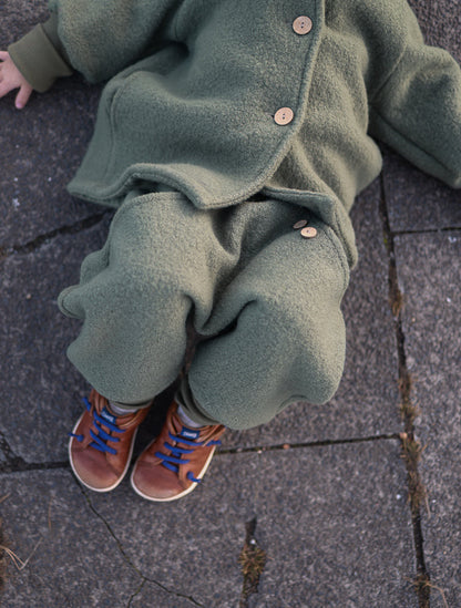 petit cochon Wichteljacke aus olivgrünem Wollwalk mit Bio-Jersey-Futter und Holzknöpfen an einem Kind