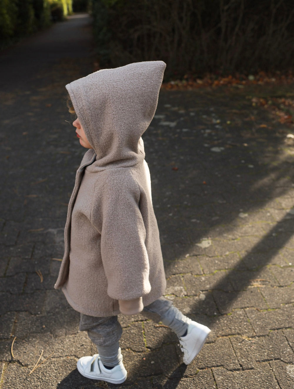 Kind trägt eine beige petit cochon Wichteljacke aus Wollwalk mit spitzer Kapuze beim Spaziergang im Freien