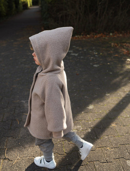 Kind trägt eine beige petit cochon Wichteljacke aus Wollwalk mit spitzer Kapuze beim Spaziergang im Freien