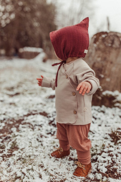 Babyknicker Kaschmir-Mix - Zimt: Baby in warmer Kaschmir-Mix-Hose mit Klappbündchen, steht im Schnee. Kombiniert mit passendem Loopbody für optimalen Komfort und Wärme.