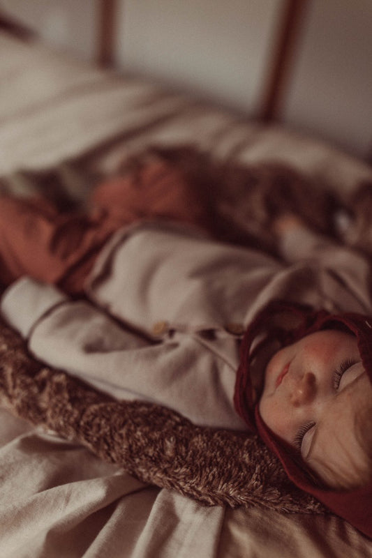Ein Baby schläft auf einem Bett, gekleidet in den Babyknicker Kaschmir-Mix - Zimt mit Klappbündchen, der Komfort und Wärme bietet. Ideal ergänzt durch den passenden Loopbody. Erstausstattung Baby und Geschenk für Babys.