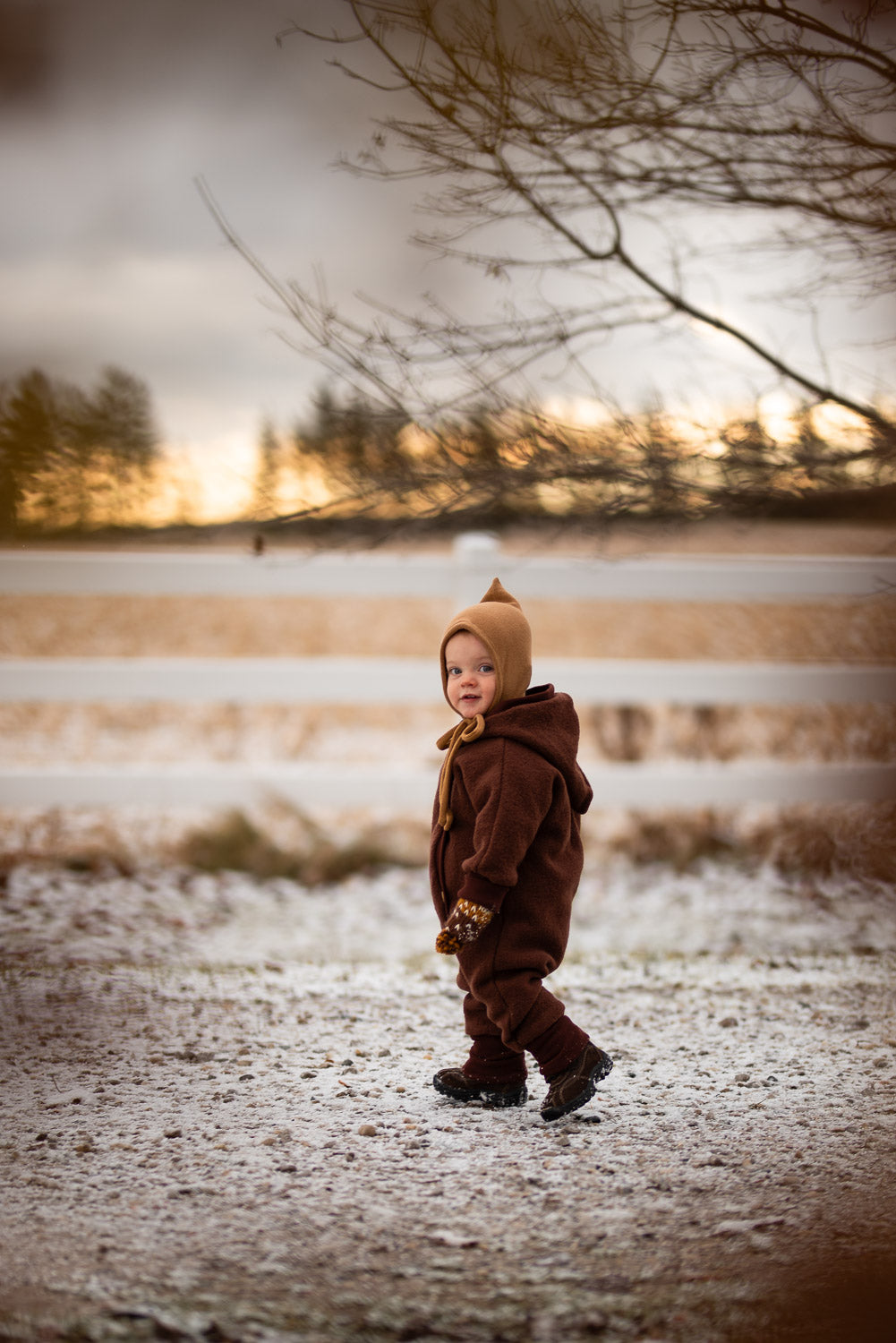 Enfant en combinaison douillette en laine bouillie Teddy – châtaigne, marchant dans la neige. La combinaison offre chaleur et liberté de mouvement, idéale pour les froides journées d’hiver.