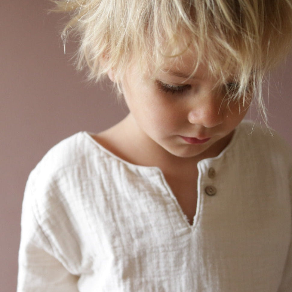 Niño lleva camisa de muselina, camisita de muselina natural. La ropa infantil está hecha de algodón orgánico y es transpirable y cómoda.
