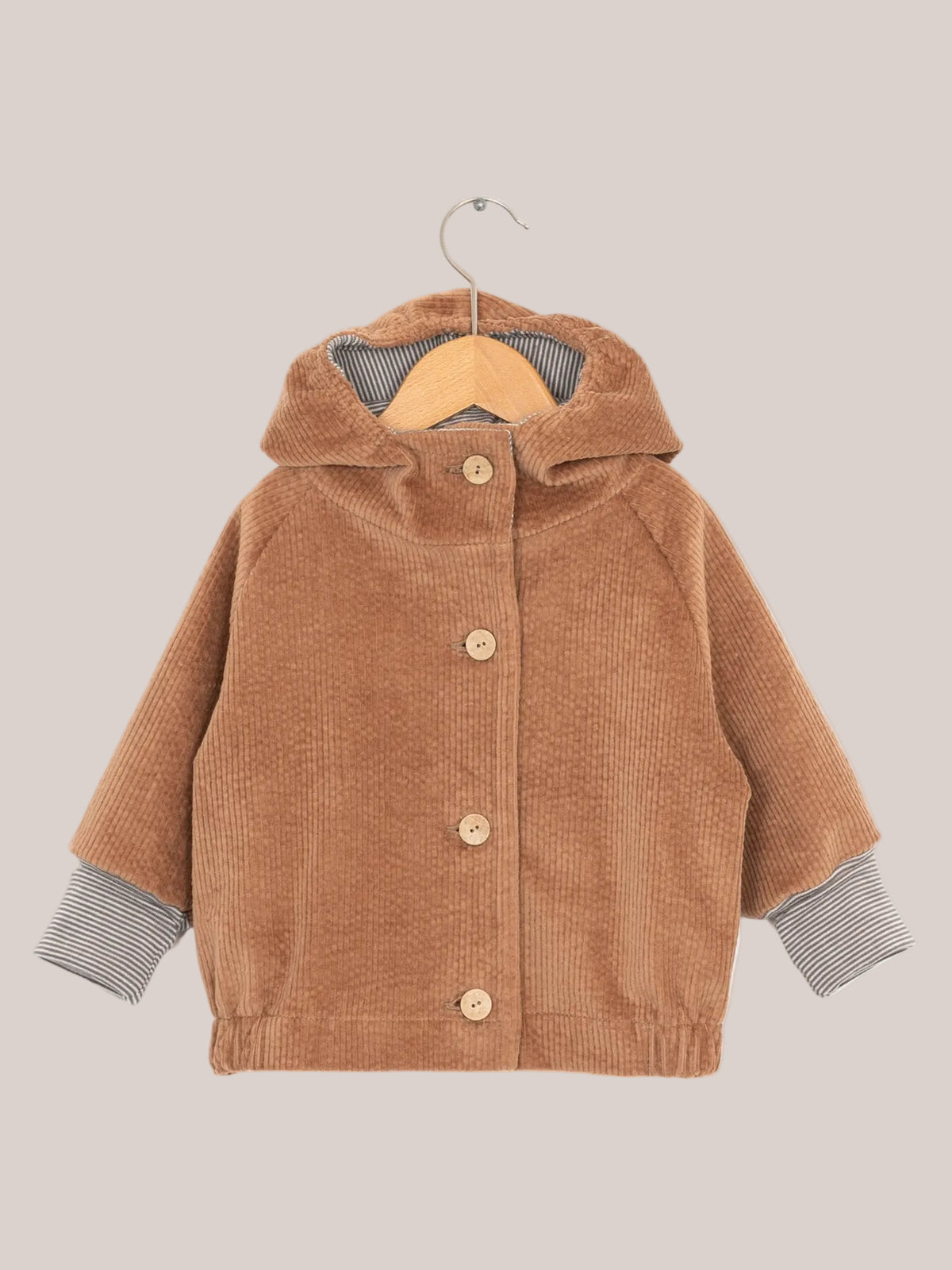 Wichteljacke Breitcord - Weizen: Braune Cordjacke mit gestreifter Kapuze und krempelbaren Ringel-Armbündchen, auf einem Kleiderbügel präsentiert.
