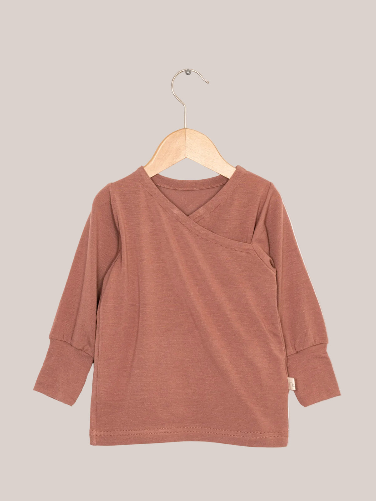 Wickelshirt aus Kaschmir-Mix - Zimt, präsentiert auf einem Holz-Schwinger. Kuschelweich, elastisch, atmungsaktiv, ideal als Shirt oder Unterhemd für Kinder.