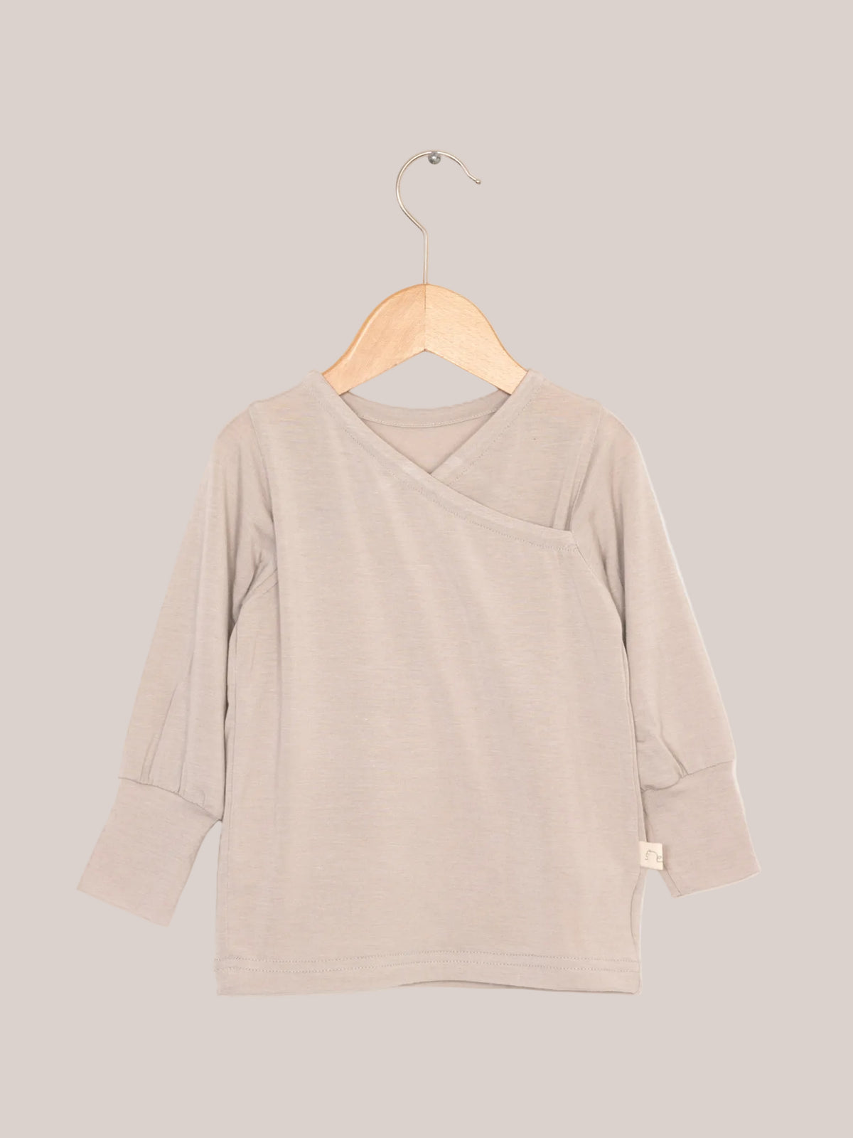 Wickelshirt aus Kaschmir-Mix - Sand auf Holzkleiderbügel, zeigt weiche, elastische Struktur und krempelbare Bündchen. Ideal als Shirt oder Unterhemd.