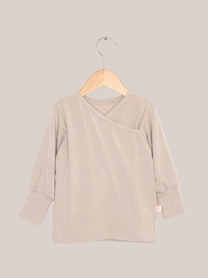 Wickelshirt aus Kaschmir-Mix - Sand auf Holzkleiderbügel, zeigt weiche, elastische Struktur und krempelbare Bündchen. Ideal als Shirt oder Unterhemd.