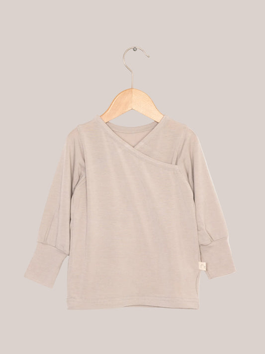 Wickelshirt aus Kaschmir-Mix - Sand auf Holzkleiderbügel, zeigt weiche, elastische Struktur und krempelbare Bündchen. Ideal als Shirt oder Unterhemd.
