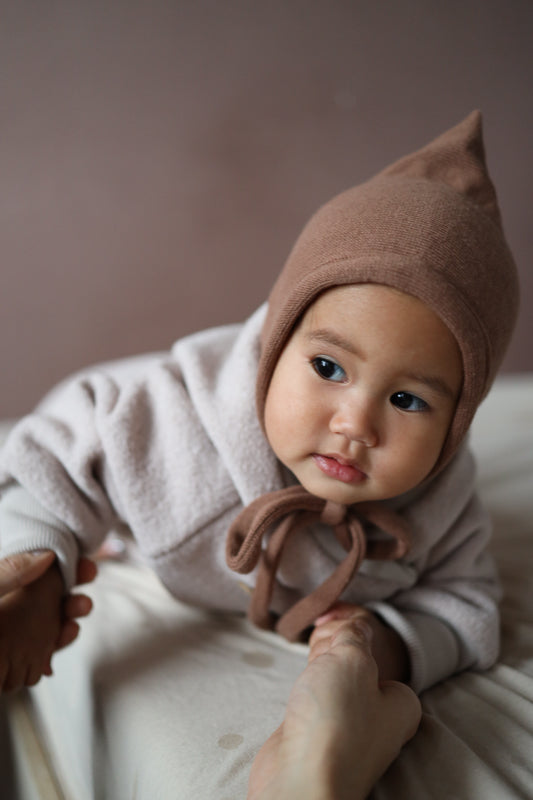 Il bambino indossa il berretto da nano in maglia – Nougat, morbidissimo e confortevole, realizzato in cotone riciclato con laccetti, perfetto per gli outfit autunnali e invernali. Primo corredino per neonati. Regali perfetti per neonati.